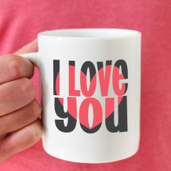 Man in pink shirt holding coffee mug with I love you block out design