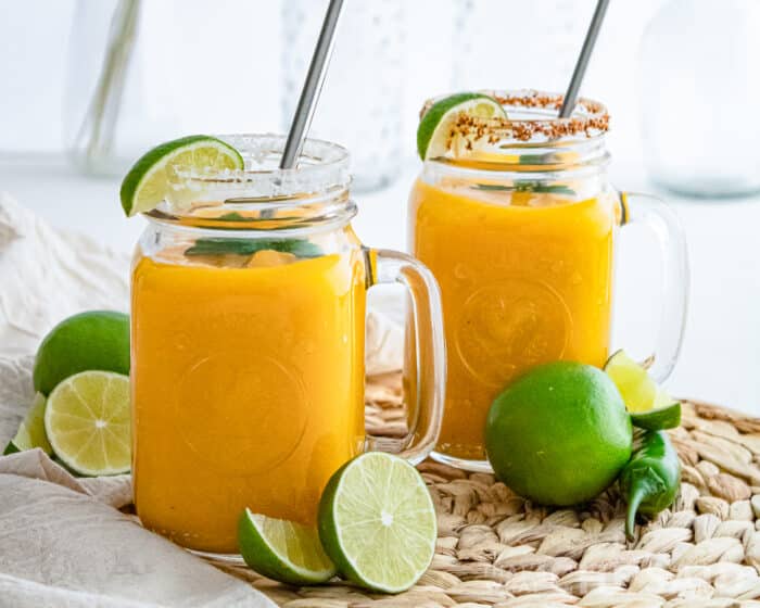 Veritcal shot of two Frozen mango margaritas with lime garnish on seagrass mat